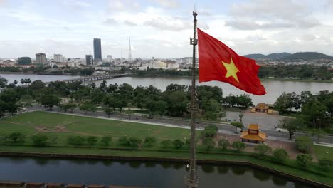 360-aerial-shot-around-the-Vietnamese-flag-in-Hué,-Vietnam-on-a-beautiful-day-in-lush-greenery