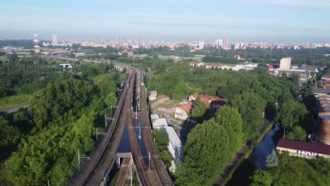 Subway-train-heading-towards-Milan-city,-aerial-fly-backward-view