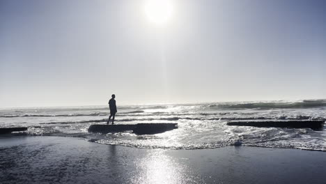 Silhouette-Eines-Mannes,-Der-Am-Ufer-Mit-Plätschernden-Wellen-Am-Strand-In-Der-Region-Taranaki-In-Neuseeland-Steht