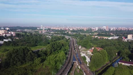 Railway-track-intersection-with-skyline-of-Milan-city,-aerial-view