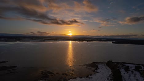 Aerial-timelapse-shot-at-sunset-over-a-lake-with-a-snow-covered-shore