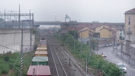 Colorful-cargo-train-leaving-suburbs-of-Milan,-back-view