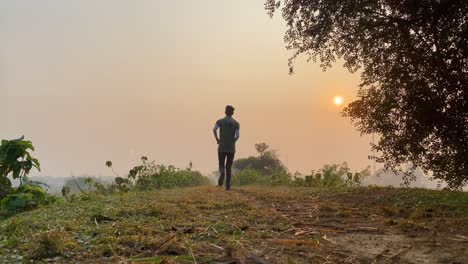 Slow-motion-runner-walking-away-from-camera-in-rural-landscape,-foggy-sunset