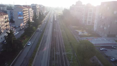 Passenger-train-entering-city-of-Milan,-aerial-view-fly-backward-with-lens-flare