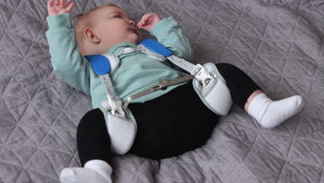 Tired-baby-girl-wearing-Pavlik-Harness-to-correct-Hip-Dysplasia-lies-on-quilt