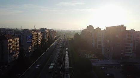Sunset-over-living-district-and-leaving-subway-train,-aerial-drone-view