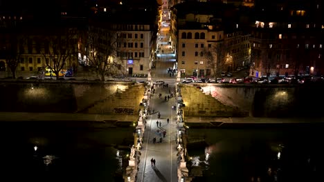 People-and-couples-walking-across-Sant'Angelo-old-Roman-bridge-with-statues-on-the-sides-at-night