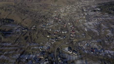 Drone-view-of-a-small-farming-community-in-the-valley-below-a-mountain-range-lined-with-pine-trees-and-snow-covered-ground
