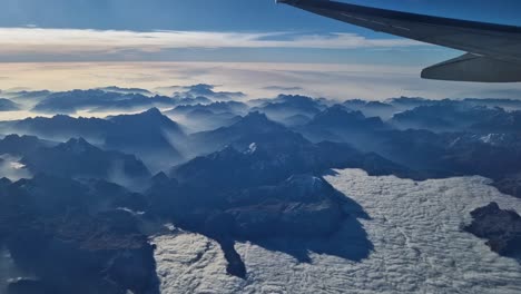 Foggy-snow-covered-Alps-from-plane,-visible-wing