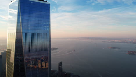 The-Upper-bay-and-the-WTC-tower,-sunrise-in-Manhattan,-NY---reverse,-aerial-view