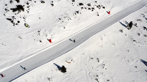 Aerial-view-over-people-skiing-down-a-mountain-ski-slope,-on-a-sunny-winter-day,-in-Slovakia