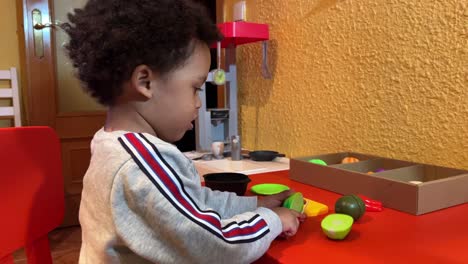 Adorable-two-year-old-black-baby,-mix-raced,-chopping-vegetables-in-his-toy-kitchen-at-home