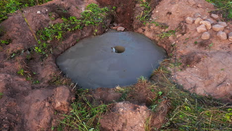 Cement-foundation-laid-for-smokehouse,-worker-digging-hole-for-pipe-with-shovel