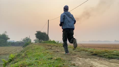 Man-jogging-at-rural-road-during-sunrise,-gas-plant-smoke-polluting-environment
