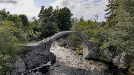 Ruin-of-medieval-ancient-Stone-Packhorse-Bridge-over-Dulnain-river,-Carrbridge,-Scotland,-UK-with-strong-water-flow