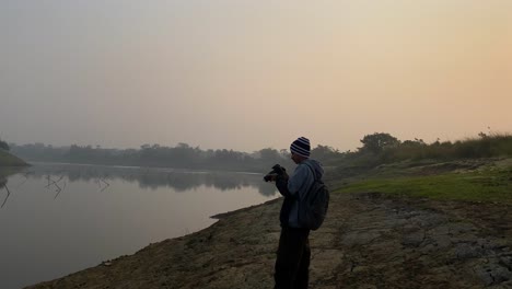 Young-photographer-with-hat-takes-pictures-of-polluted-river-in-Sylhet,-dolly-in