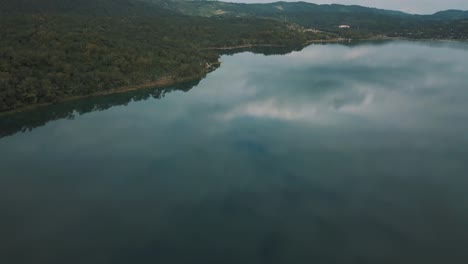 Drone-Aéreo-Volando-Sobre-Hermoso-Lago-Cristalino-Reflectante-En-Peten-Itzá,-El-Remate,-Guatemala