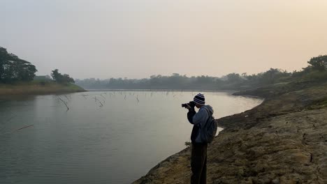 Photographer-capturing-polluted-river-on-foggy-day-with-camera,-wide-view