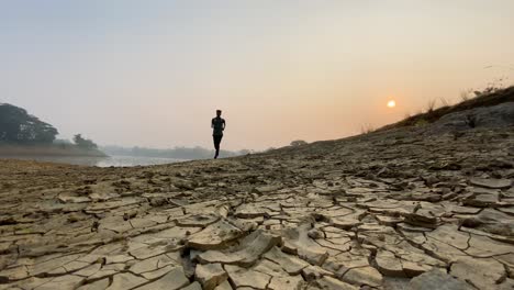 Wide-shot-of-active-runner-man-jogging-in-countryside-dry-land,-foggy-sunrise-in-winter-morning