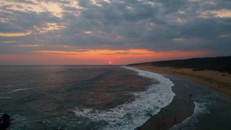 Cinematic-drone-pullback-from-the-beautiful-setting-sun-on-the-horizon-to-reveal-the-Caribbean-sea-and-the-beach-of-Puerto-Escondido-with-tourist-swimming-and-enjoying-the-amazing-view-of-the-sunset