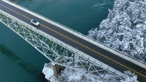 Overhead-view-of-cars-driving-across-a-bridge-with-snow-covering-the-land