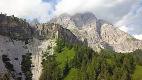 Fly-over-green-mountain-with-pine-tree-forest-on-a-cliff-and-mountain-peaks,-National-Park-Tre-Cime,-Belluno,-Italy
