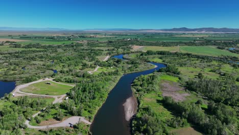 River-Flowing-Through-Green-Fields-In-Saint-Anthony,-Idaho,-United-States---aerial-drone-shot