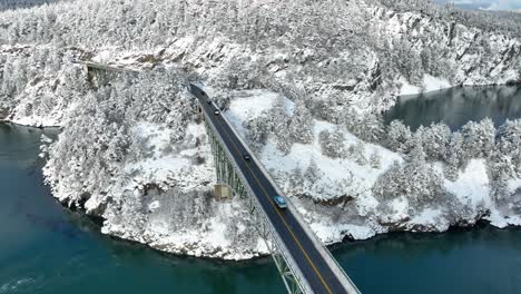 Drone-shot-of-cars-driving-across-a-bridge-with-snow-blanketing-the-land