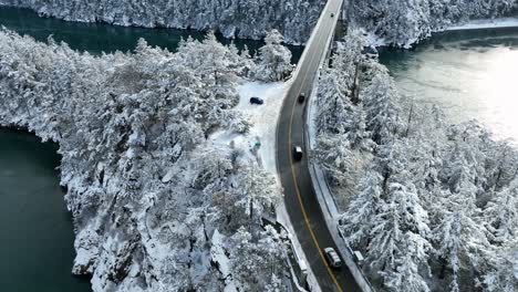 Aerial-view-of-cars-driving-over-water-with-snow-surrounding-the-land