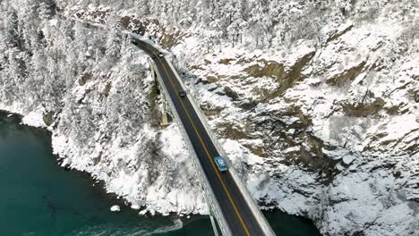 Drone-shot-of-cars-driving-over-onto-the-mainland-covered-in-snow