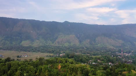 Aerial-shot-flying-over-trees-to-fields-and-small-villages-below-big-hills-on-Samosir-Island-in-Lake-Toba-in-North-Sumatra,-Indonesia