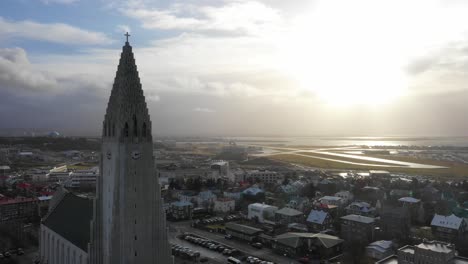 Majestic-Hallgrimskirkja-Reykjavík-Cathedral-During-a-magnificent-Sunset-over-church-tower-and-airport,-Aerial-to-sun