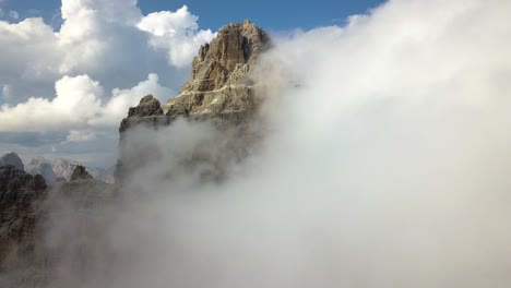 A-mountain-peak-being-covered-by-fluffy-white-clouds,-closeup-aerial-flight-view-of-Drei-Zinnen-National-Park,-Monte-Paterno,-Dolomiti,-Italia