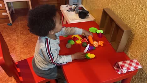 Exotic-and-sweet-two-year-old-black-baby,-mix-raced,-plays-to-chop-vegetables-in-his-new-toy-kitchen-at-home