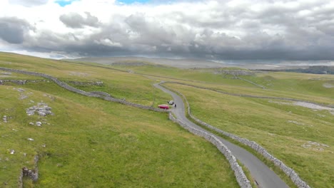long-paved-road-alongside-bumpy-green-hills-atop-Malham-Cove,-North-Yorkshire,-England-on-cloudy-day