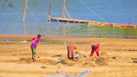 Child-and-woman-working-on-coastal-soil-in-Bangladesh,-handheld-view