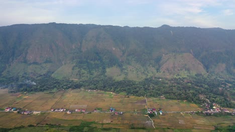 Backwards-aerial-shot-of-village-and-fields-on-Samosir-Island-in-Lake-Toba-in-North-Sumatra,-Indonesia
