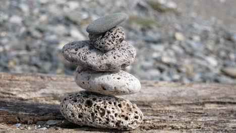 Small-textured-beach-rocks-balanced-zen-like-on-wooden-beach-sleeper-closeup-left-dolly