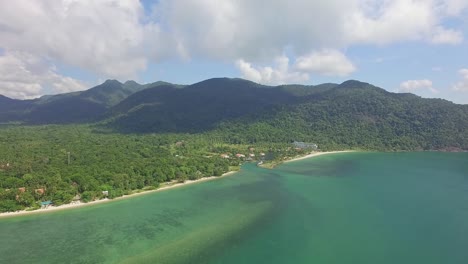 Aerial-back-tracking-shot-of-a-tropical-beach-on-Koh-Chang-showing-mountains-with-lush-dense-Jungle-and-a-sea-view