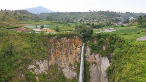 Aerial-view-of-Sipiso-Piso-Waterfall-in-North-Sumatra,-Indonesia---drone-flying-up-and-away