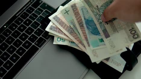 Man-put-polish-banknotes-with-black-wallet-on-laptop,-polish-money-and-national-currency