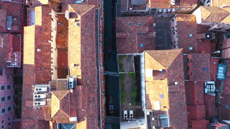 Aerial-top-down-view-flying-over-canal-and-roofs-while-gondola-is-passing-by-on-a-sunny-day-in-Venice-in-Italy-in-4k