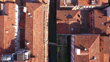 Static-aerial-top-down-view-of-canal-and-roofs-while-gondola-passing-by-on-a-sunny-day-in-Venice-in-Italy-in-4k