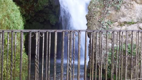 Metal-guard-railing-with-idyllic-rural-splashing-waterfall-flowing-in-background