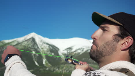 Close-up-shot-of-a-fly-fisherman-casting-his-lure-in-front-of-gorgeous,-snow-capped-mountains