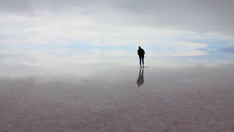 Lone-silhouetted-female-walks-on-etheral-Uyuni-salt-flats-with-mirror-effect