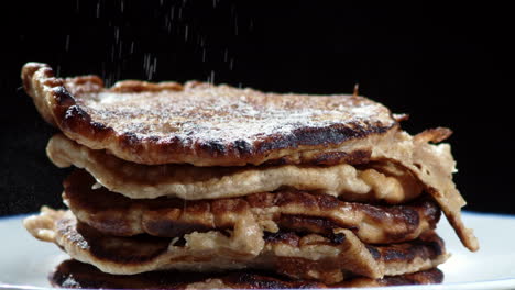 Close-up-of-icing-sugar-being-sprinkled-over-a-stack-of-freshly-baked-pancakes