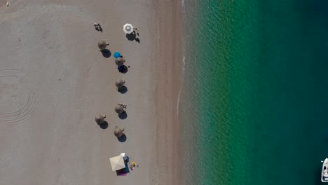 Quiet-sandy-beach-with-umbrellas-on-shoreline-near-calm-turquoise-sea-water,-vacation-in-Mediterranean