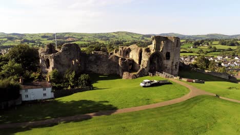 Ancient-Welsh-landmark-Denbigh-Castle-medieval-old-hill-monument-ruin-tourist-attraction-aerial-rising-countryside-view