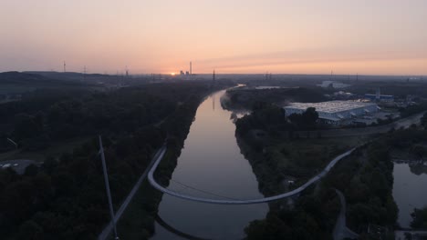 Sunrise-over-Grimberger-Sichel-Pedestrian-Bridge-on-Rhine-Herne-Canal-in-Germany,-Aerial-Drone-View